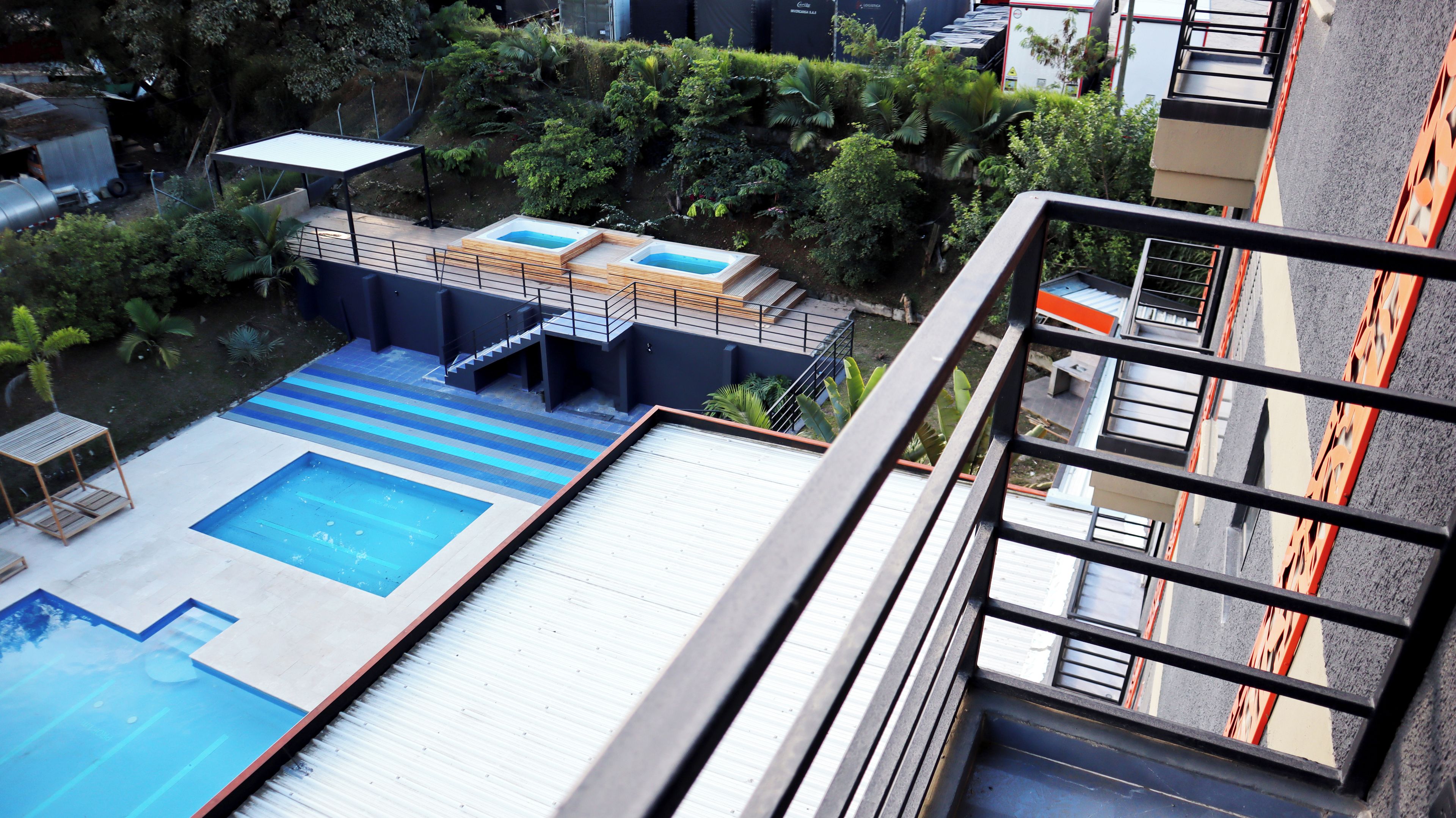 A rooftop swimming pool with a wooden deck and a small hot tub.