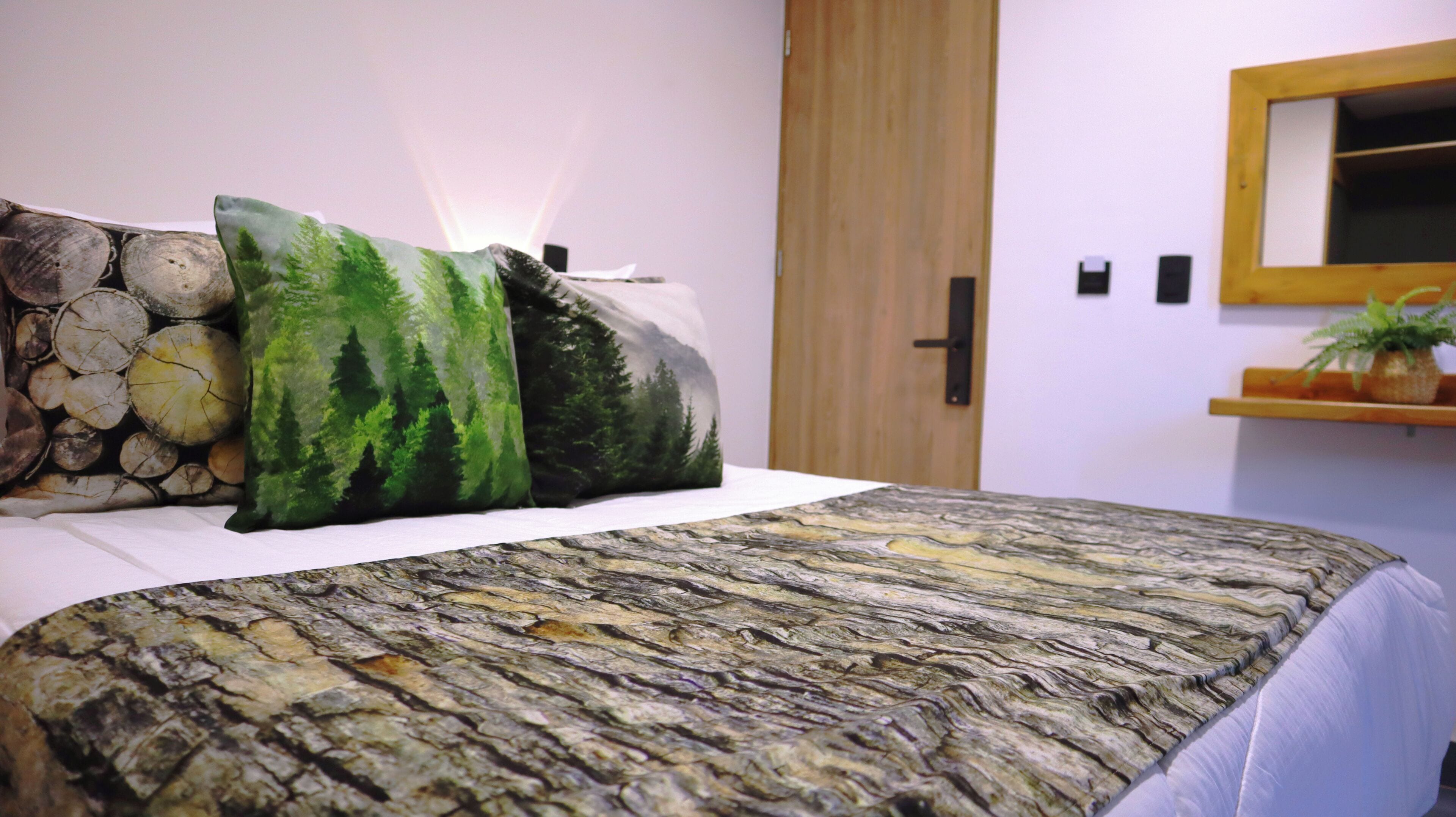 Una cama con colcha de motivos forestales, almohadas con diseño de bosque y un espejo adosado a la pared.