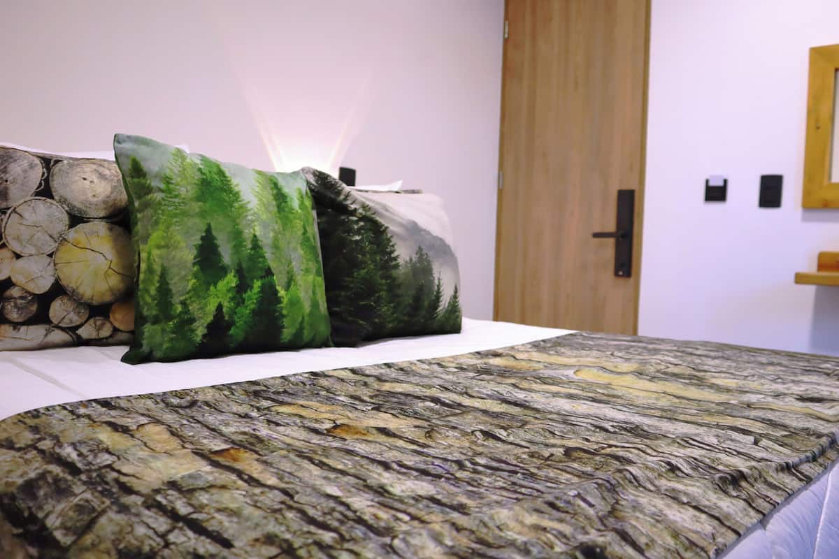 Una cama con colcha de motivos forestales, almohadas con diseño de bosque y un espejo adosado a la pared.