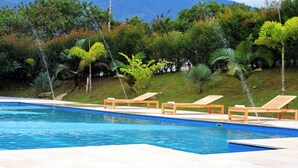 A swimming pool with wooden loungers and a grassy slope with trees in the background. - GIO GREEN HOTEL GIRARDOTA MEDELLIN (Girardota)