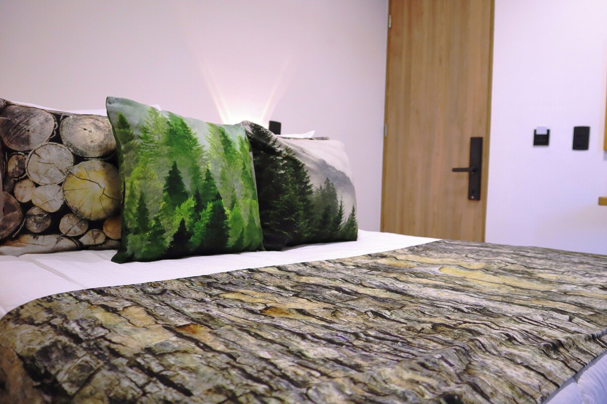 Ein Bett mit Bettwäsche und Kissen im Waldmotiv, sowie ein wandmontierter Spiegel.