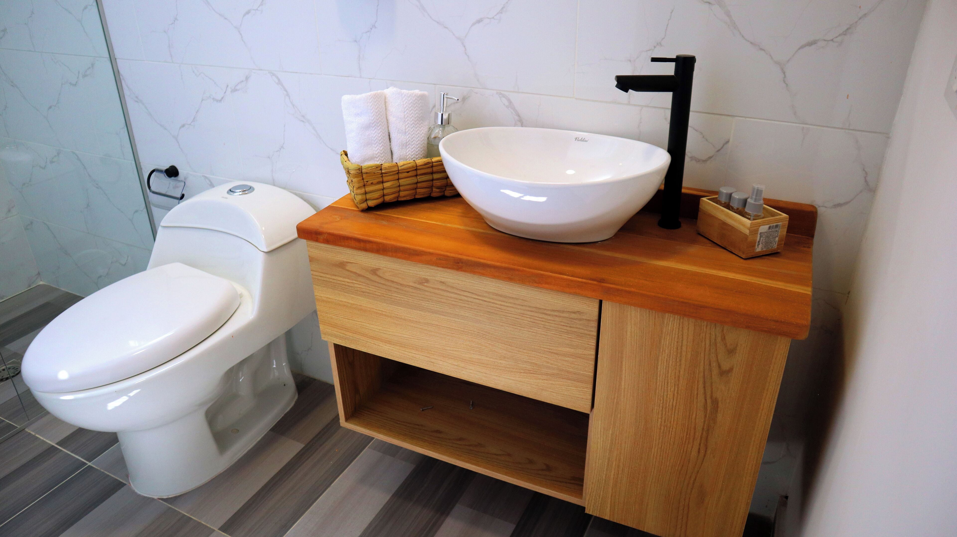A bathroom with a white toilet, a wooden vanity with a white sink, and a marble-tiled wall.