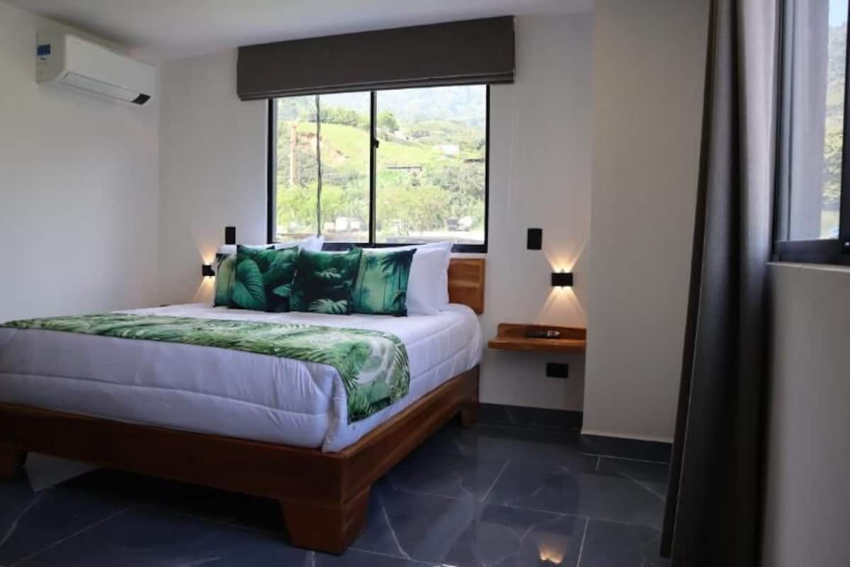 Un dormitorio con cama, ventana, mesita de noche y aire acondicionado de pared.