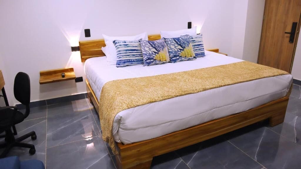 Un dormitorio con cama, mesitas de noche, una silla y una puerta de madera.