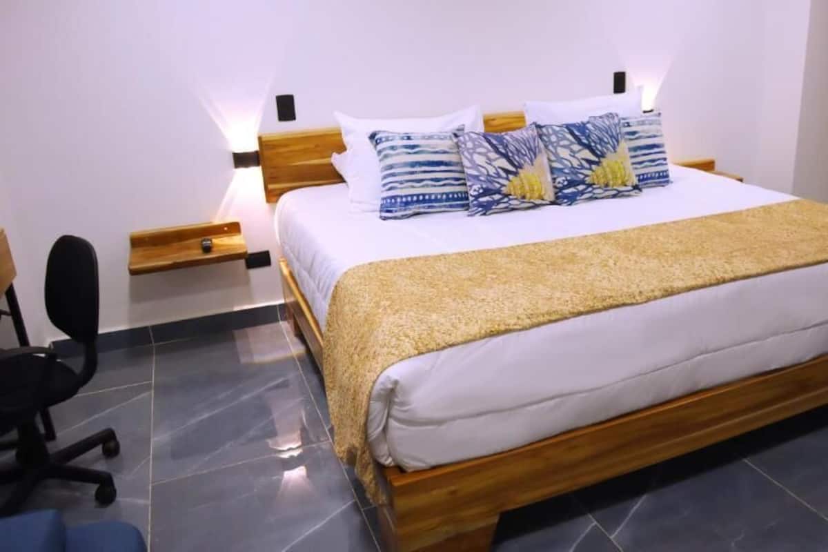 Un dormitorio con cama, mesitas de noche, una silla y una puerta de madera.