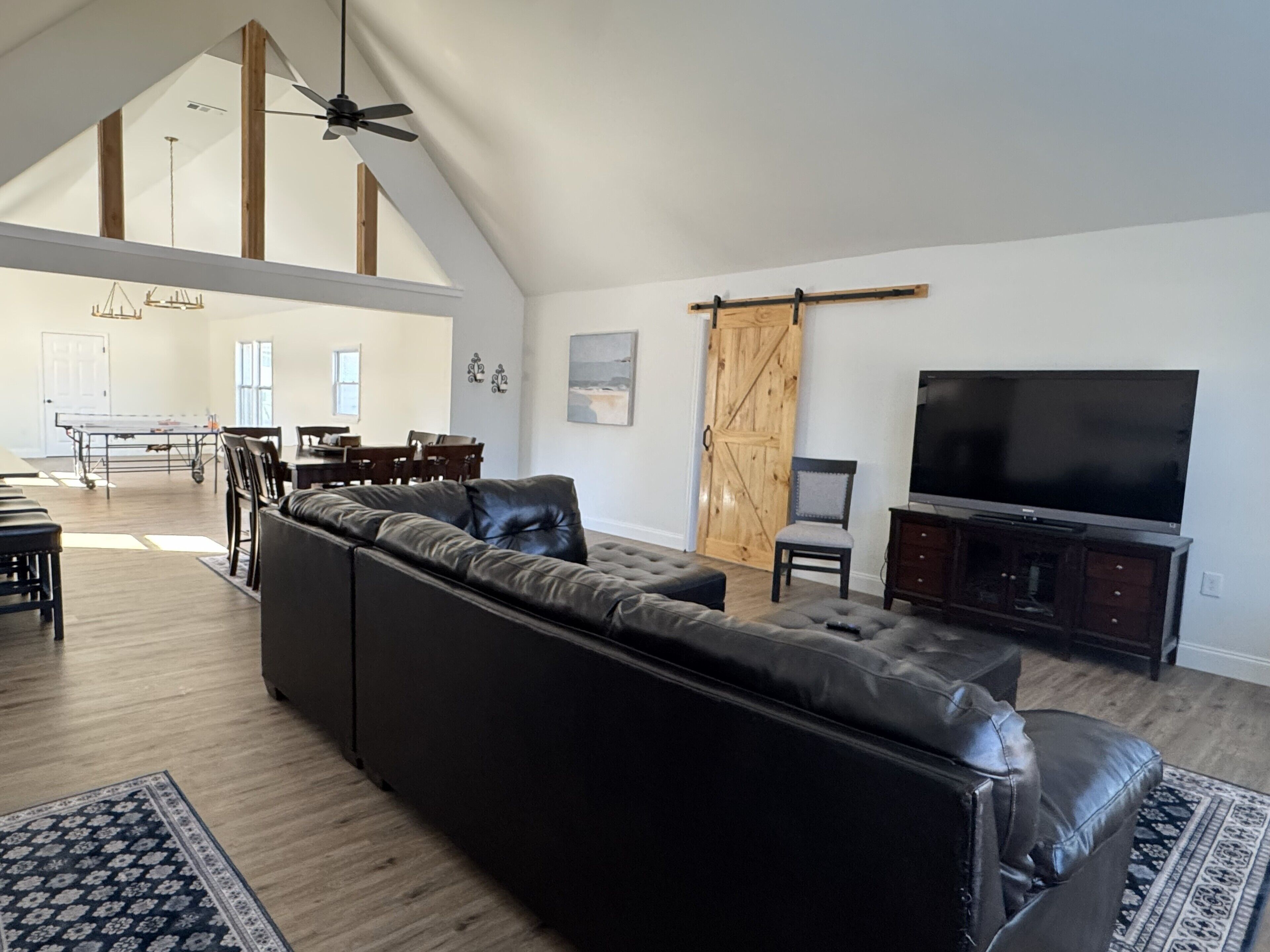 A spacious living room with a large black leather sectional sofa, a flat-screen TV, and a dining area with a table and chairs.