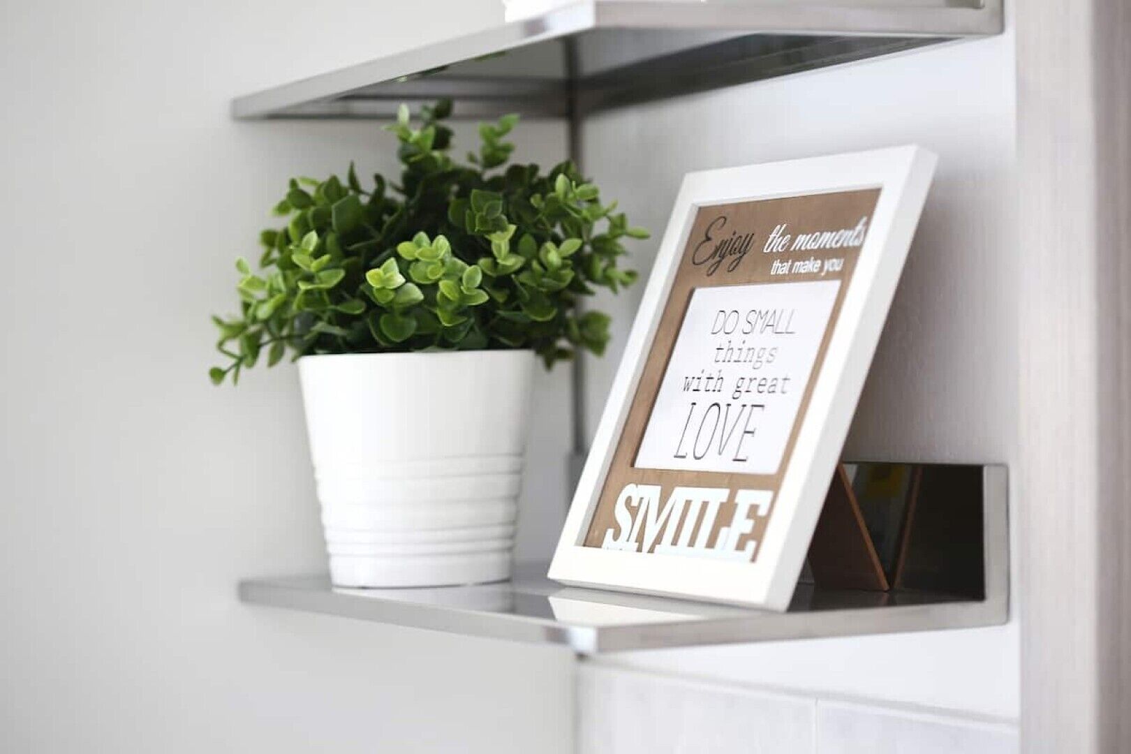 En inramad, inspirerande citattext står på en hylla, och bredvid den finns en krukväxt.