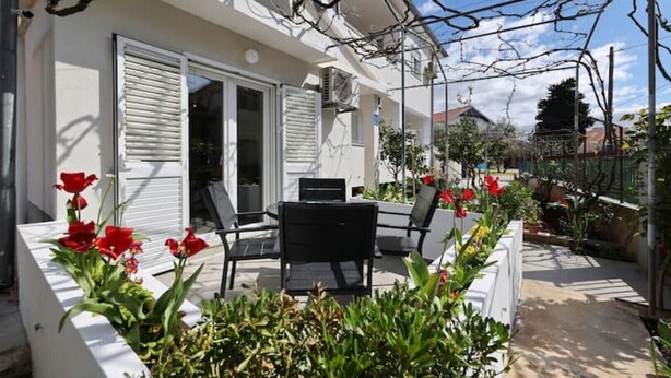 Ein Haus mit Terrasse, Tisch und Stühlen sowie roten Blumen.