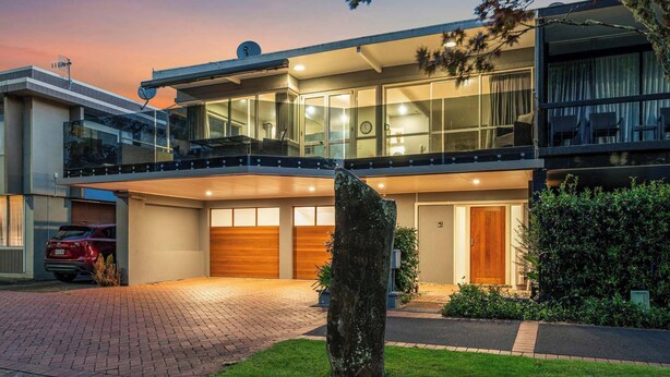 Ein modernes, zweistöckiges Haus mit Garage, großen Fenstern und einem gepflegten Rasen.