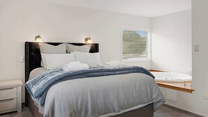 Ein modernes Schlafzimmer mit Bett, Nachttischen, einem Fenster mit Jalousien und einem integrierten Waschbecken.