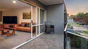 Ein Balkon mit einer Couch, einem Sessel und einem Fernseher im Hintergrund.