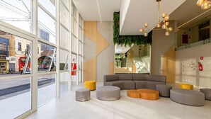A modern interior with large windows, a sectional sofa, and a unique ceiling light fixture. - Studio com Sacada no Centro - Man1706 (Curitiba)