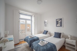 Ein Hotelzimmer mit zwei Betten, einem Fenster, einer Tür und einem kleinen Tisch mit einer Lampe.