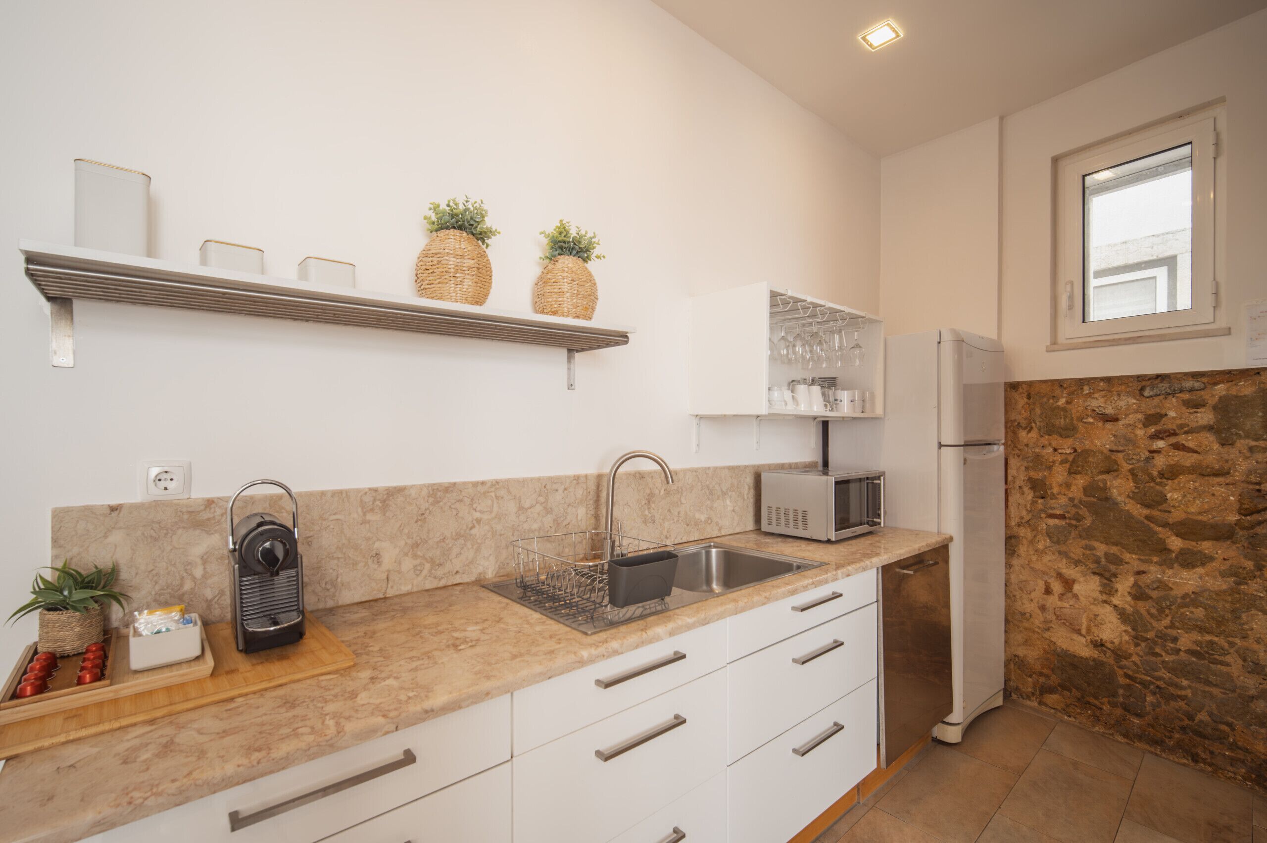 Una cocina moderna con armarios blancos, encimera de granito, microondas integrado, pileta de acero inoxidable y una pared de detalles de piedra.