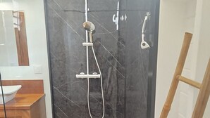 Een moderne badkamer met een glazen douchecabine, een houten bankje en een witte wastafel.