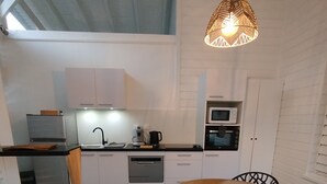 Een moderne keuken met witte kasten, een eethoek met een ronde tafel en zwarte stoelen, en een hangende lamp.