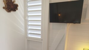 Een woonkamer met een donkerblauwe bank, een geweven mand, een aan de muur bevestigde televisie en een kleine tafel met een lamp.