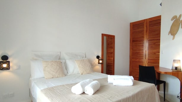 Een netjes opgemaakt bed met witte lakens en handdoeken, een houten bureau met een stoel, en een wandlamp.
