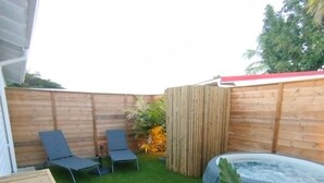 Een achtertuin met kunstgras, twee lounge stoelen, een houten omheining en een jacuzzi.