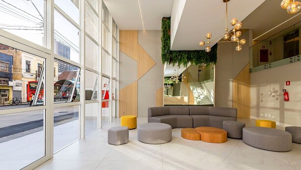 A modern interior with large windows, a sectional sofa, and a unique ceiling light fixture. - Studio em Predio Novo no Centro - Man1708 (Curitiba)