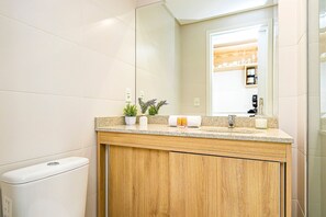 A bathroom with a wooden vanity, a sink, a mirror, and a toilet. - Studio em Predio Novo no Centro - Man1708 (Curitiba)