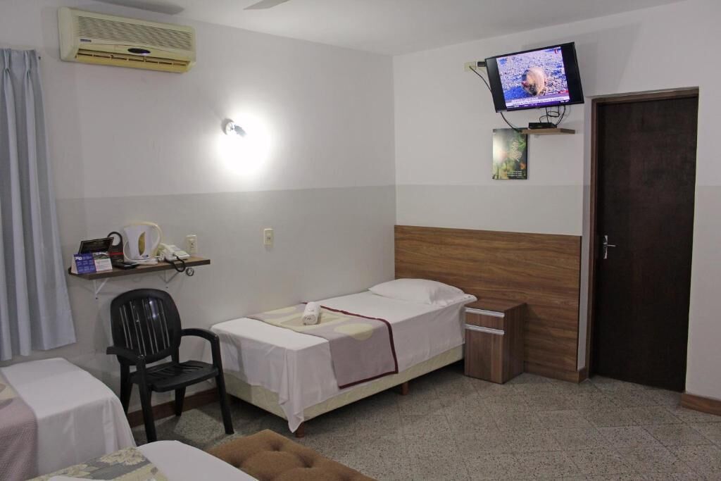 Une petite pièce propre, avec un lit simple, un bureau et une chaise, un téléviseur fixé au mur et une porte.