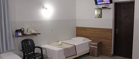 A small, clean room with a single bed, a desk with a chair, a television mounted on the wall, and a door.