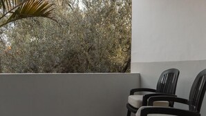 A balcony with two chairs, a white wall, and dense foliage in the background.