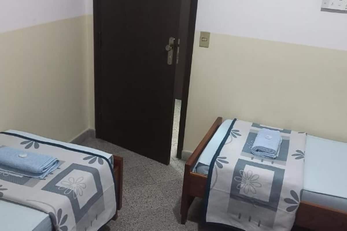 A small, simple room with two single beds, each with a patterned bedspread.