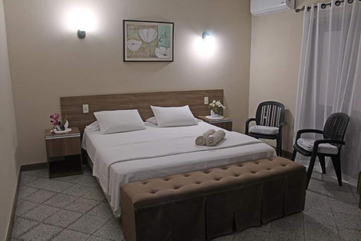 A neatly arranged hotel room with a bed, a bench, a chair, and a nightstand with a vase of flowers.