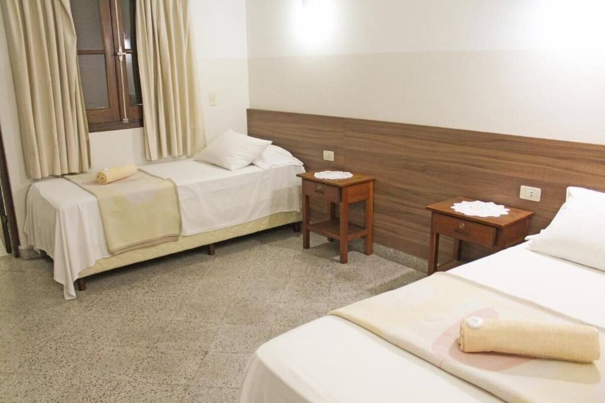 A hotel room with two beds, a wooden headboard, a small wooden nightstand, and a window with curtains.