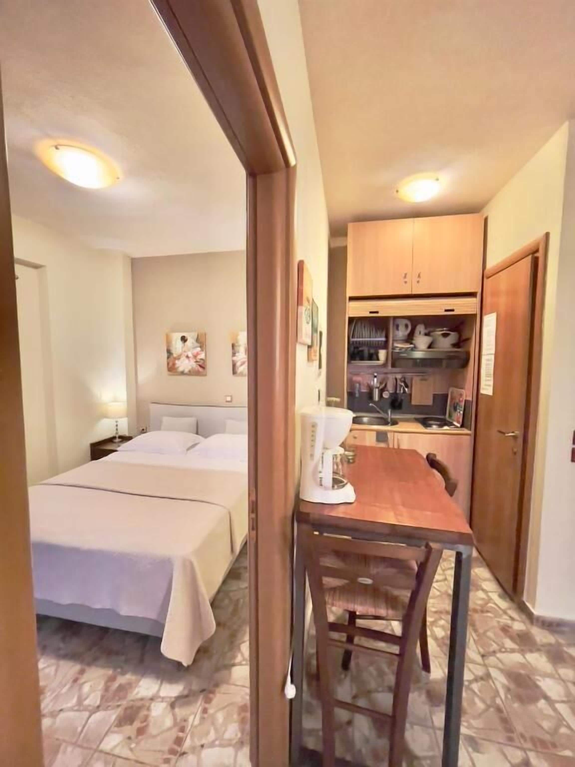 A compact hotel room with two beds, a small kitchenette, and a dining area.