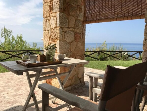 A stone pillar with a table and bench, a view of the sea, and a grassy area. - Palamidi Apartments (Kassandra)