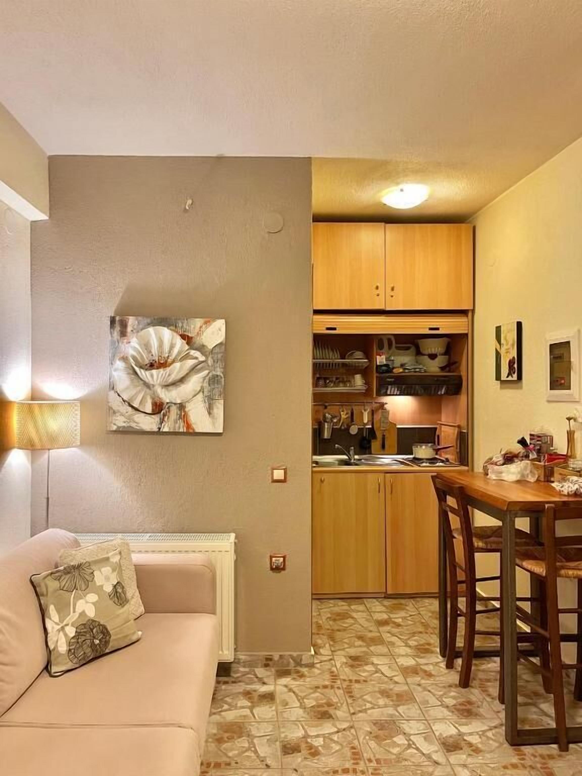 A compact living space with a kitchenette, a dining area with wooden chairs, and a sofa with a floral cushion.