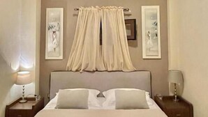 A hotel room with a large bed, two bedside tables, a ceiling light, and two wall-mounted picture frames. - Palamidi Apartments (Kassandra)