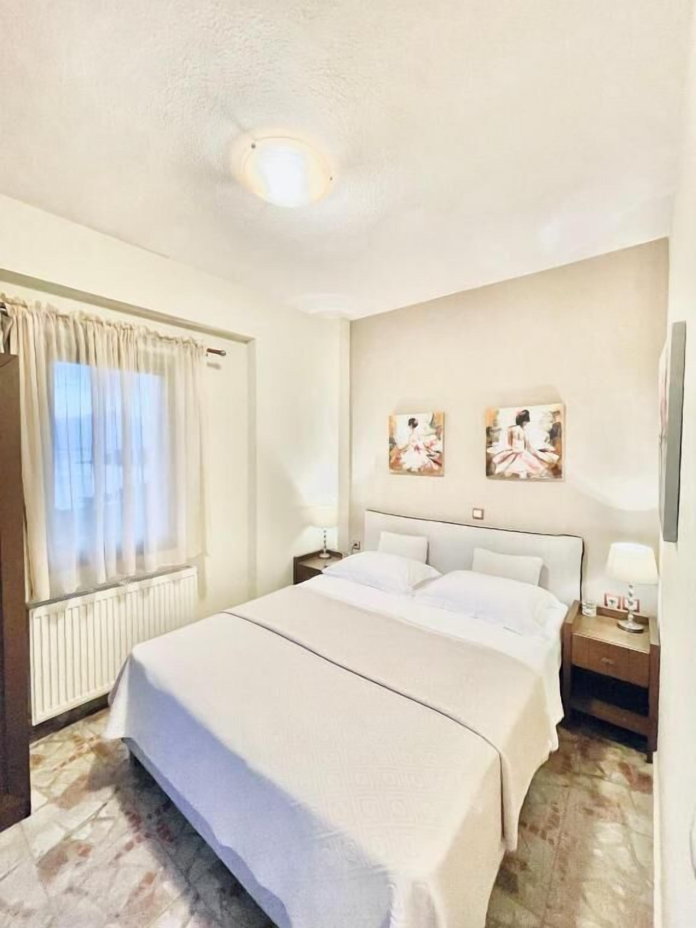 A hotel room with a double bed, a nightstand, a lamp, and two wall-mounted paintings.