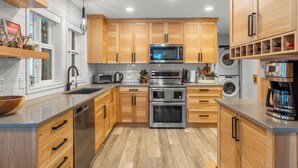 A modern kitchen with wooden cabinets, stainless steel appliances, and a built-in oven. - Modern 2 bedroom ground level suite w/ private hot tub, laundry (Vernon)