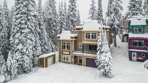 A multi-story building with a snow-covered roof and surrounding snow-laden trees. - Modern 2 bedroom ground level suite w/ private hot tub, laundry (Vernon)