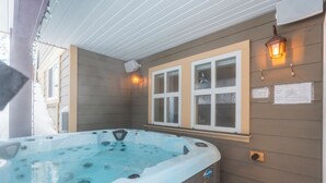 A hot tub with a wooden deck, a window with a view, and a wall-mounted light fixture. - Modern 2 bedroom ground level suite w/ private hot tub, laundry (Vernon)