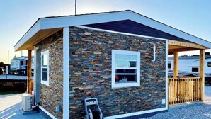 Un petit bâtiment aux murs recouverts de pierres, doté d’une terrasse en bois et d’un espace abrité.