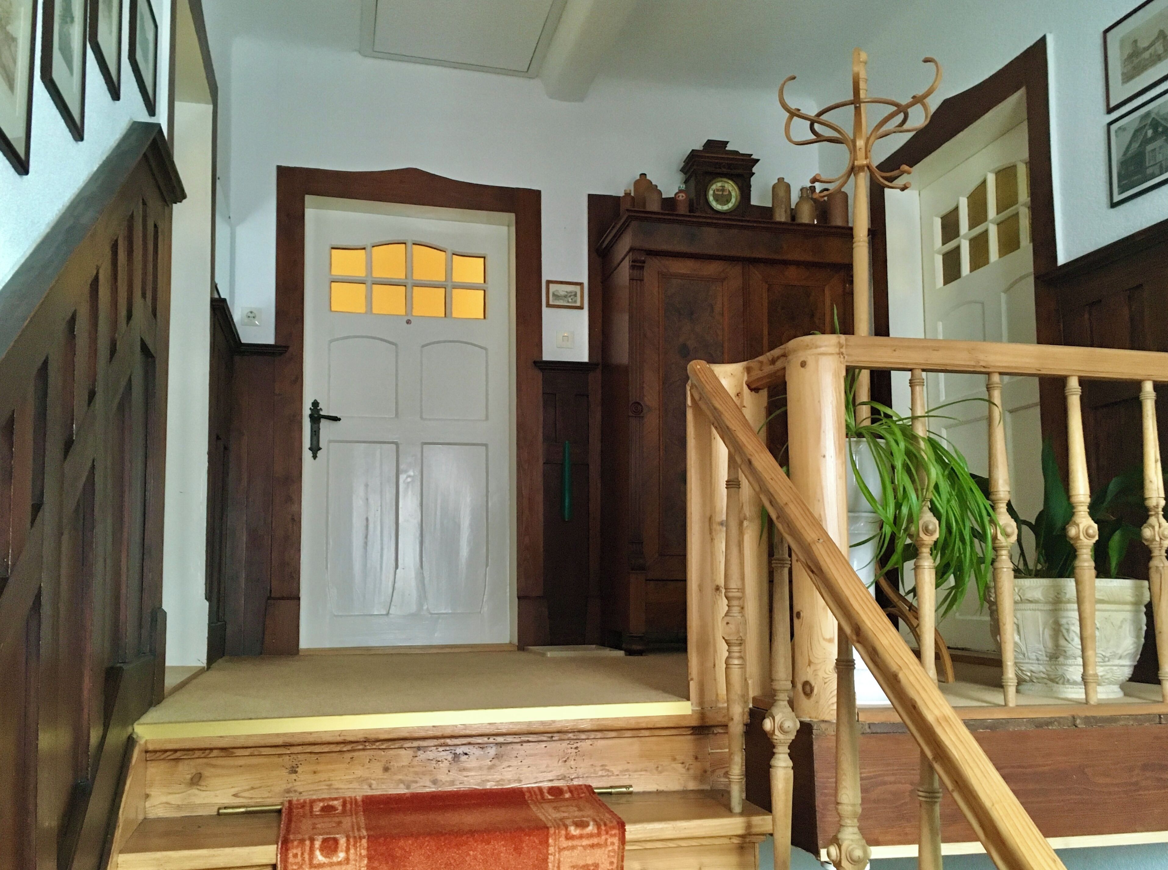 Una escalera de madera que lleva a una puerta con marco blanco y un ventanal con vidrios amarillos.