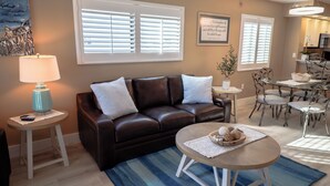 A living room with a brown leather sofa, a round coffee table, and a dining area with a table and chairs. - Panoramic Fort Myers Beachfront Condo - Private Sunset Views (Fort Myers Beach)