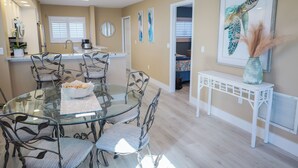 A dining area with a glass table and metal chairs, a white console table with a vase, and a framed seahorse artwork on the wall. - Panoramic Fort Myers Beachfront Condo - Private Sunset Views (Fort Myers Beach)