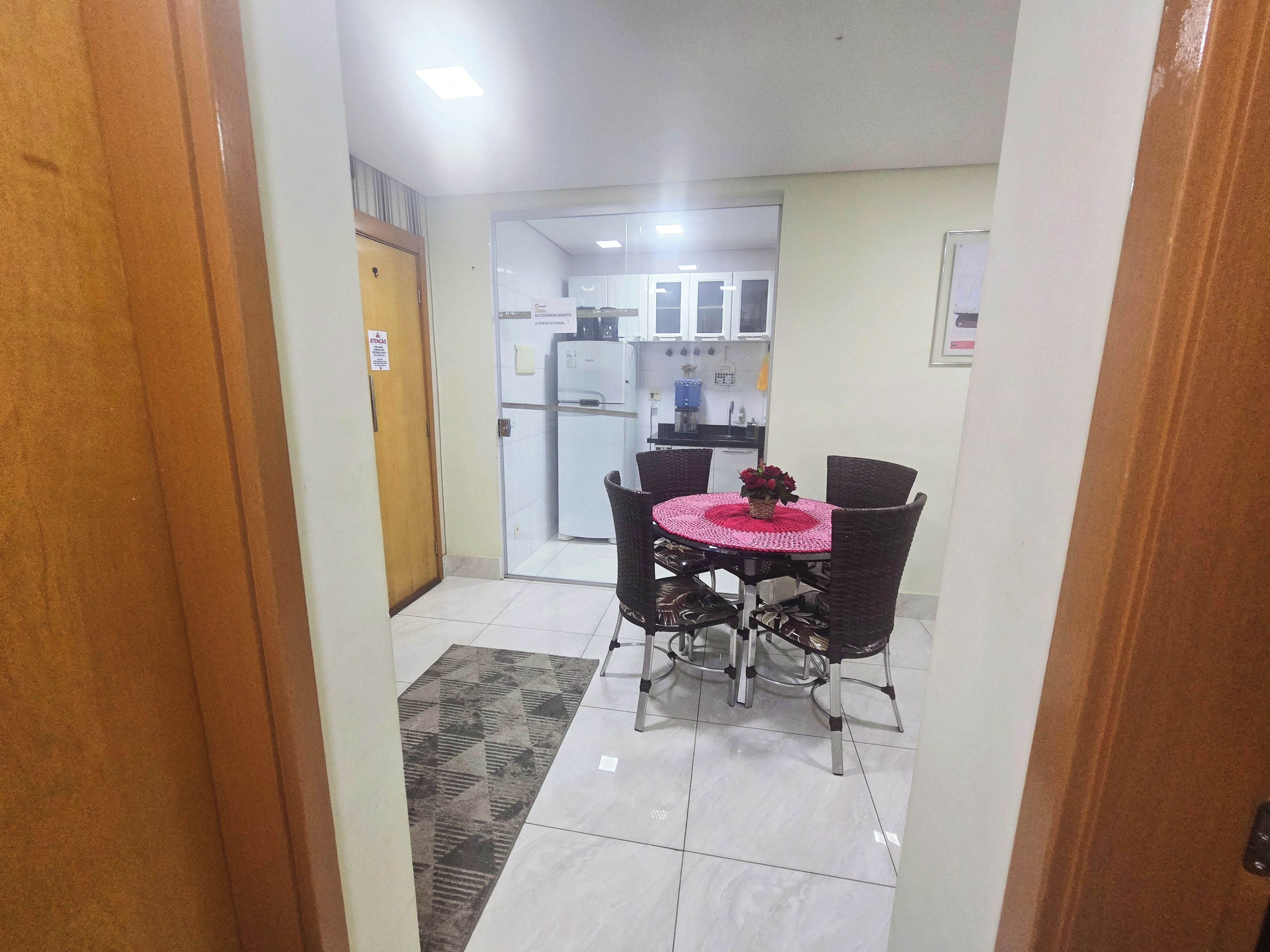 A hallway leading to a dining area with a table and chairs, a refrigerator, and a kitchen area in the background.
