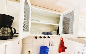 A kitchen with a coffee maker, shelves with dishes, and hanging mugs.