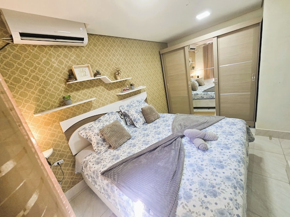 A bedroom with a bed, a wardrobe, a mirror, and a wall-mounted air conditioner.