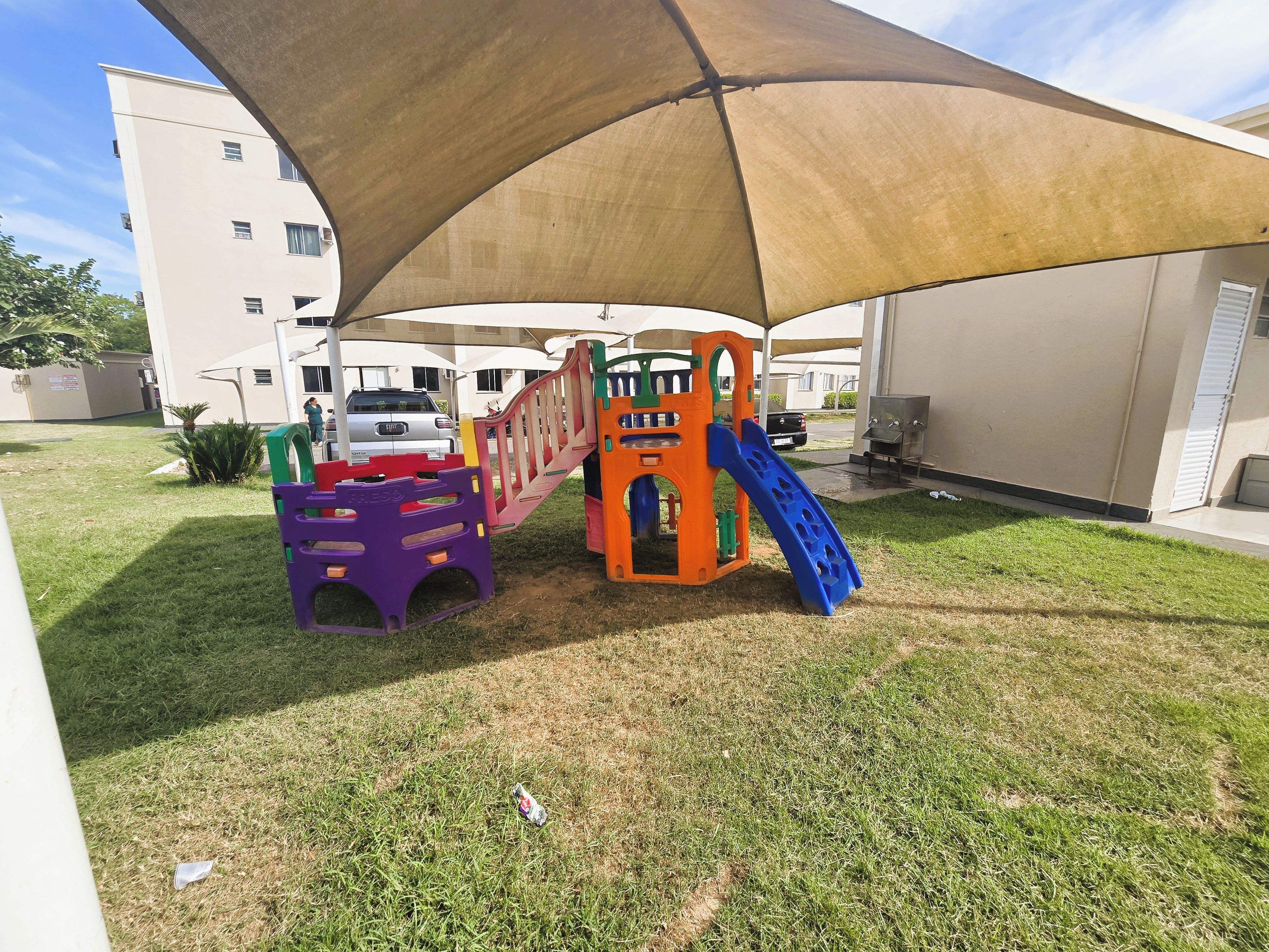 Un terrain de jeux avec un toboggan et des structures d’escalade, un espace abrité et un bâtiment en arrière-plan.