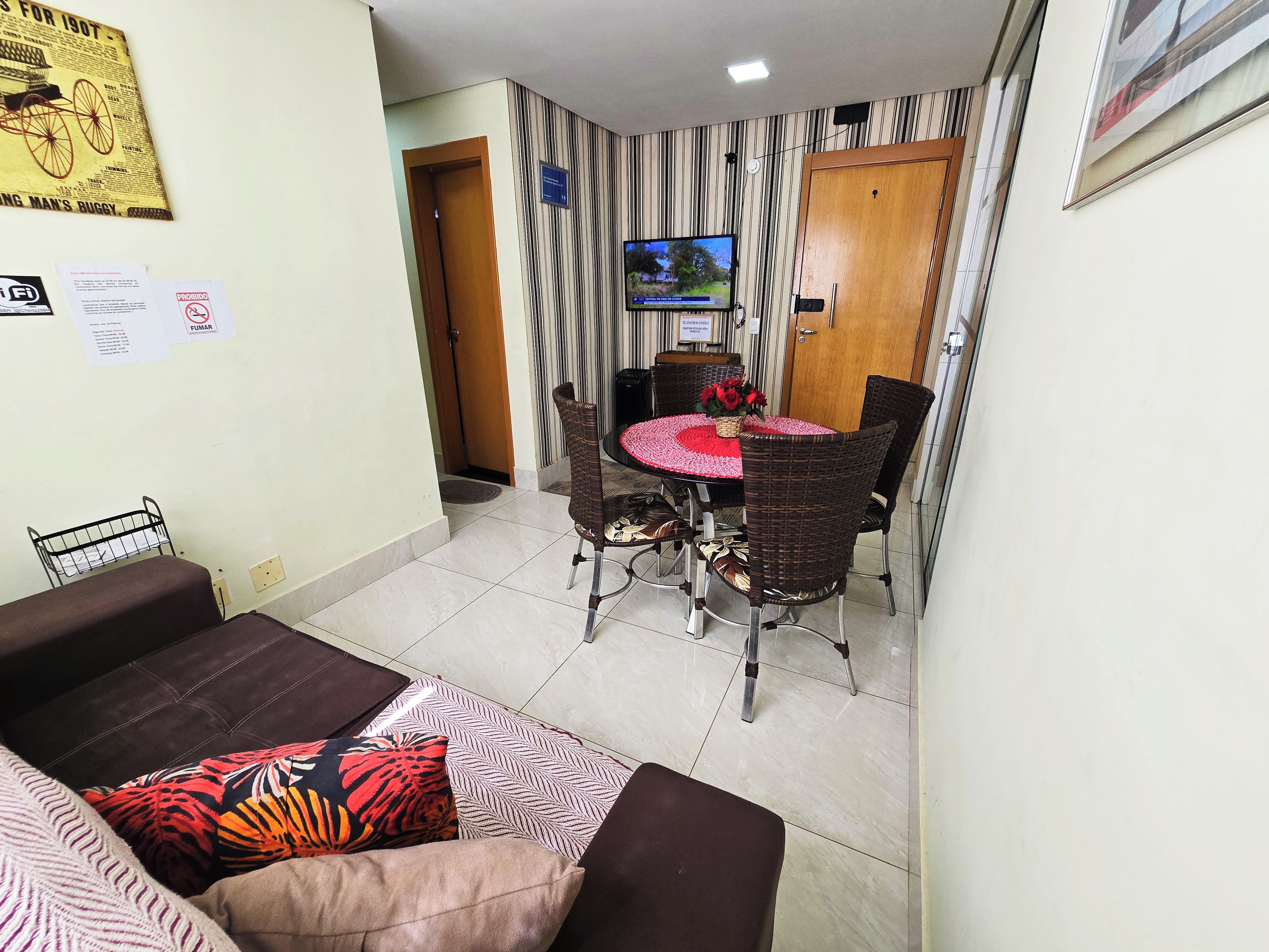 Un comedor con una mesa redonda, sillas de mimbre y un televisor montado en la pared.
