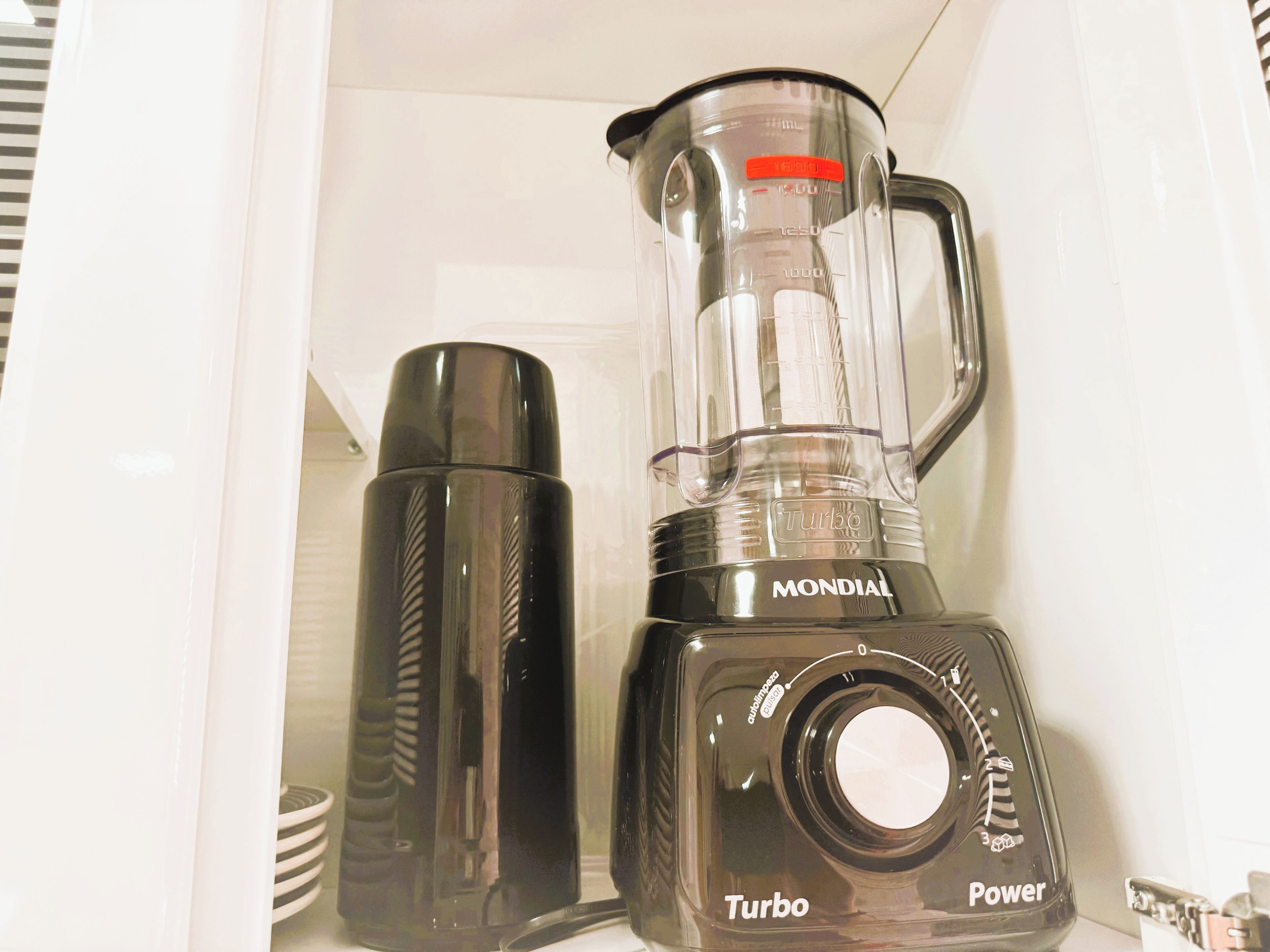 Uma área de cozinha com liquidificador e termo.