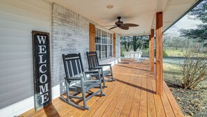 A wooden deck with rocking chairs and a 'WELCOME' sign, overlooking a grassy area.